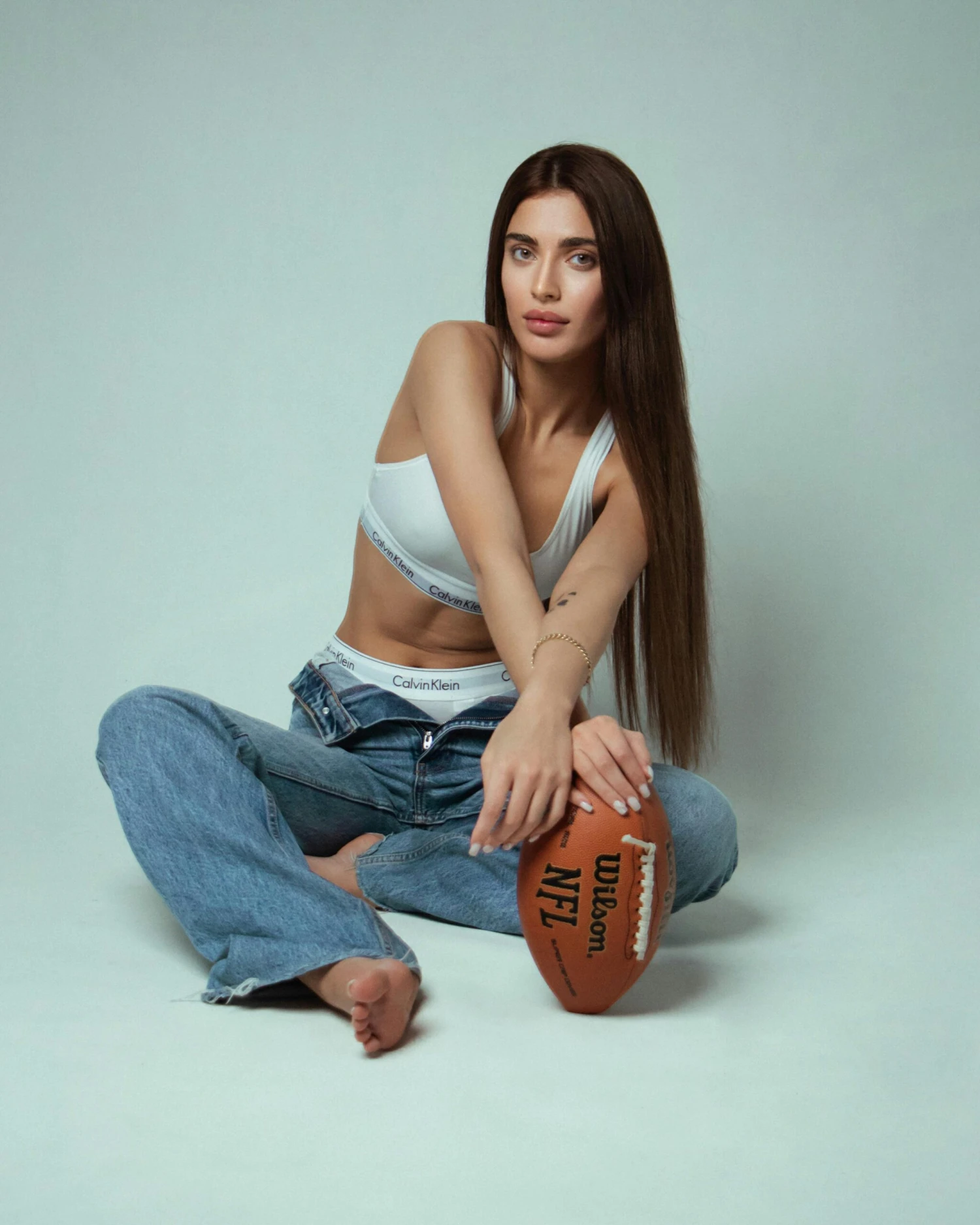 Returns & Exchanges 1 Casual portrait of a young woman in jeans holding an American football in a studio setting.